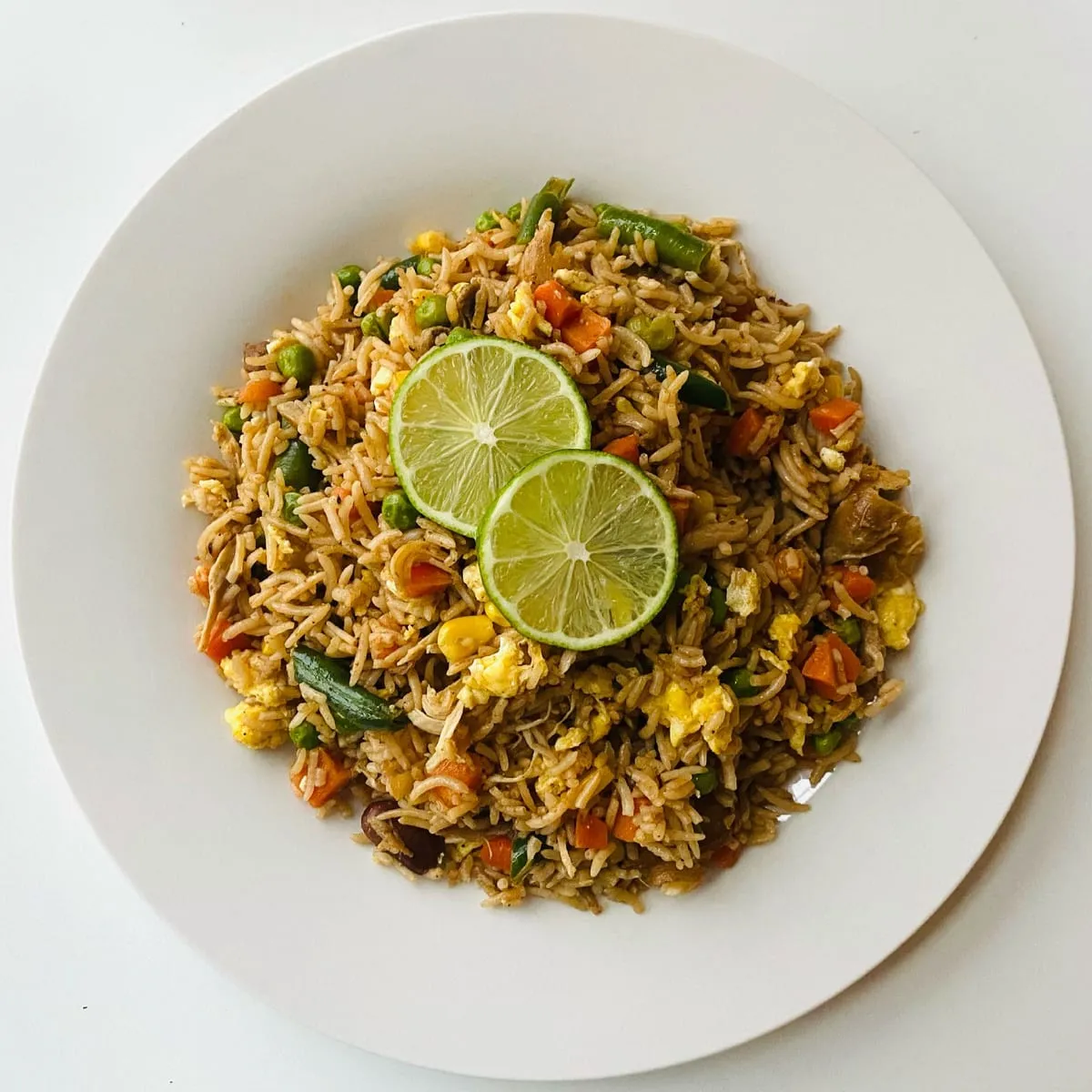 Arroz chaufa de la casa servido en plato blanco con rodaja de limón