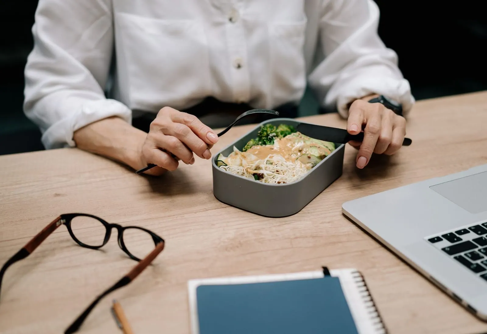 Almuerzo en táper abierto sobre un escritorio, junto a una laptop